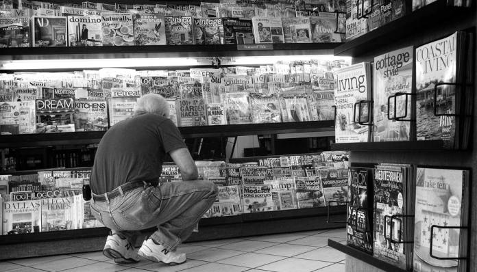 A man squatting next to a magazine rack