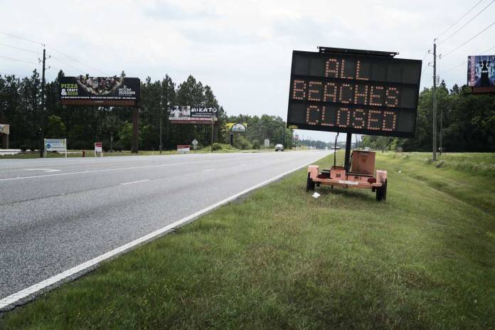 Portable sign at the edge of a highway with notification that all beaches on the Gulf Coast are closed.